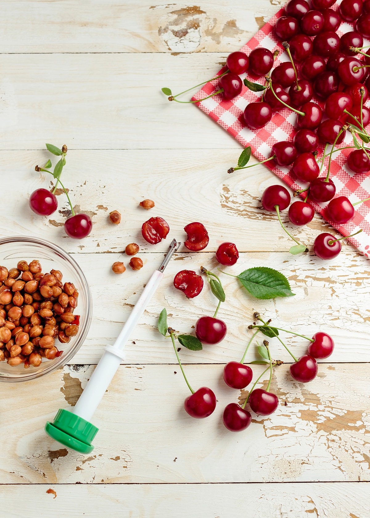 Fresh cherries on a wood table with a cherry pitter and bowl of pits