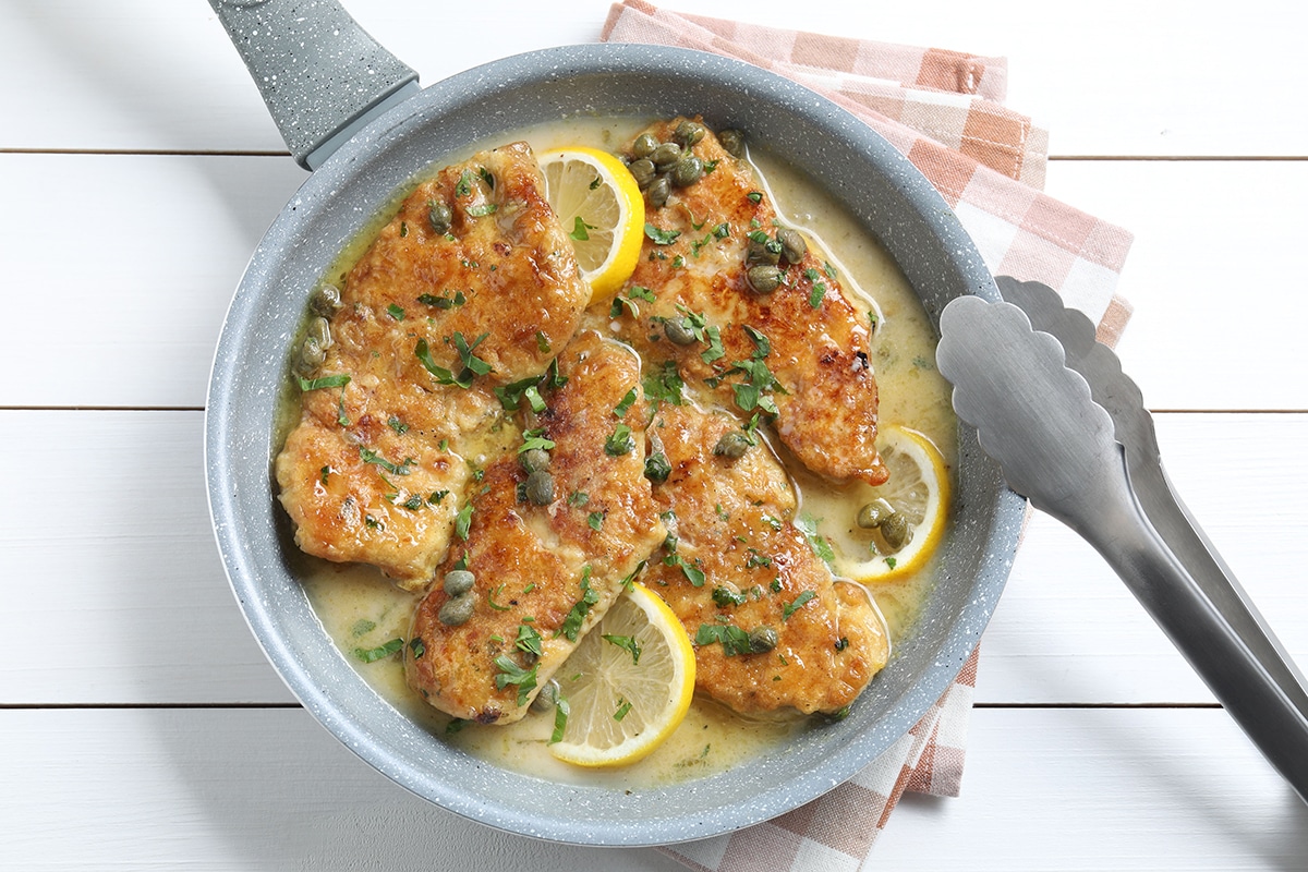 chicken with lemons in a sauce in a grey skillet with tongs
