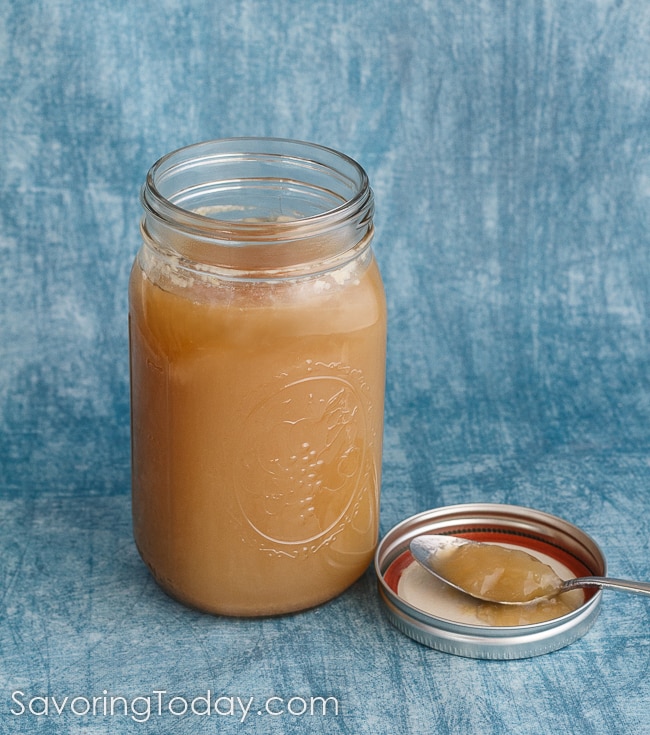 Homemade chicken stock on a spoon resting in the lid with the mason jar of stock beside it. 