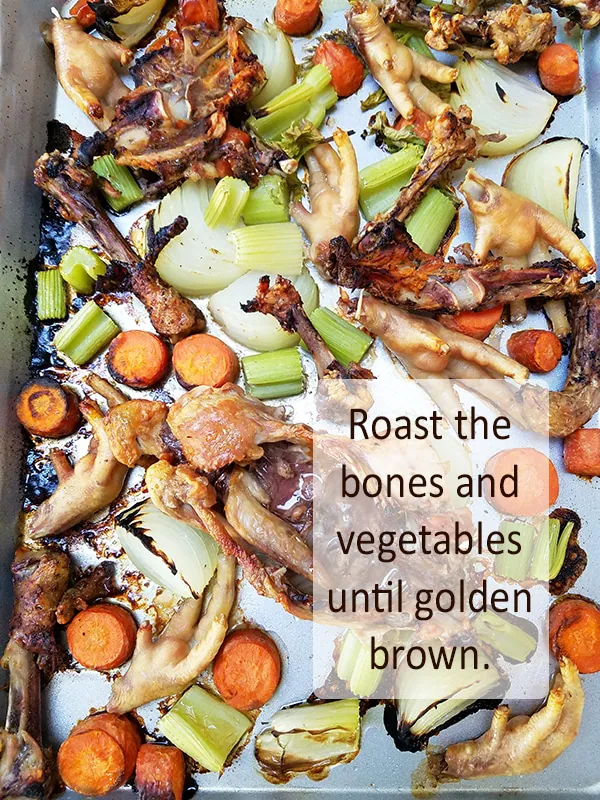 Chicken feet, bones, carrots, celery and onion roasted on a pan.
