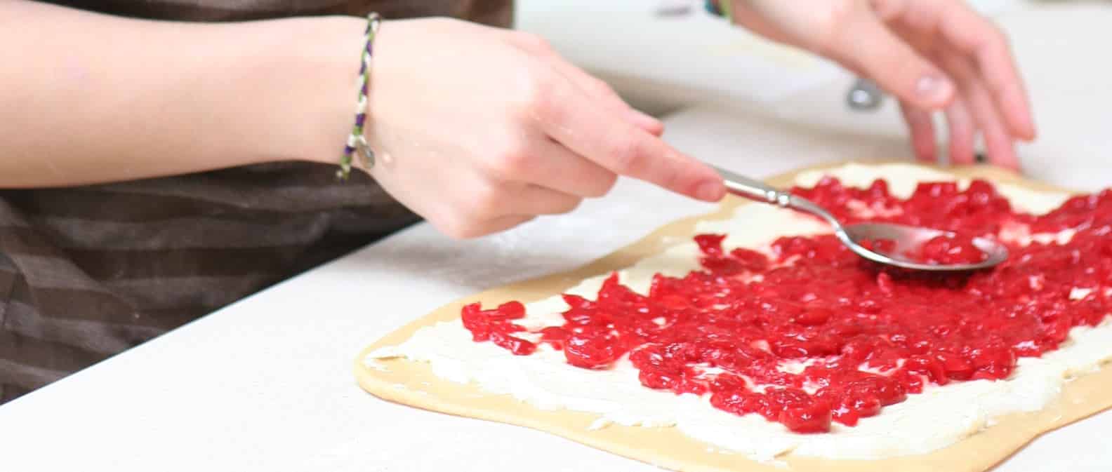 cherries spread over cream cheese filling and dough before rolling and shaping