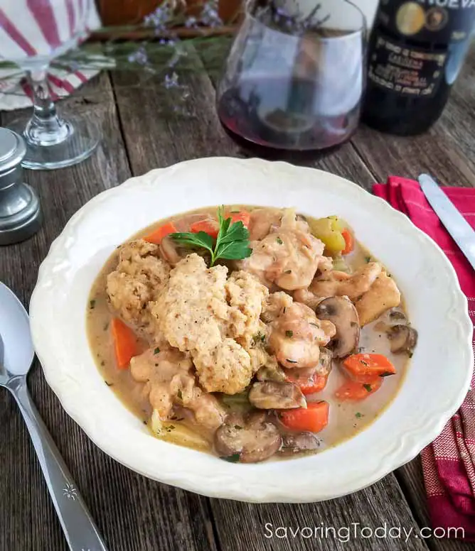 Chicken and dumplings with carrots and mushrooms served in a white bowl with a sprig of parsley.