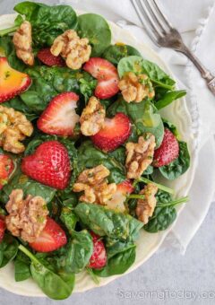 Spinach salad with sliced strawberries and walnuts in a white bowl with a napkin and fork.