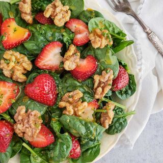 Spinach salad with sliced strawberries and walnuts in a white bowl with a napkin and fork.