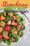 Strawberry and spinach salad with walnuts on a cream plate.