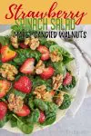 Strawberry and spinach salad with walnuts on a cream plate.