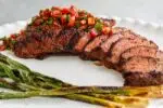 Sliced grilled tri-tip on a white platter with grilled young leeks