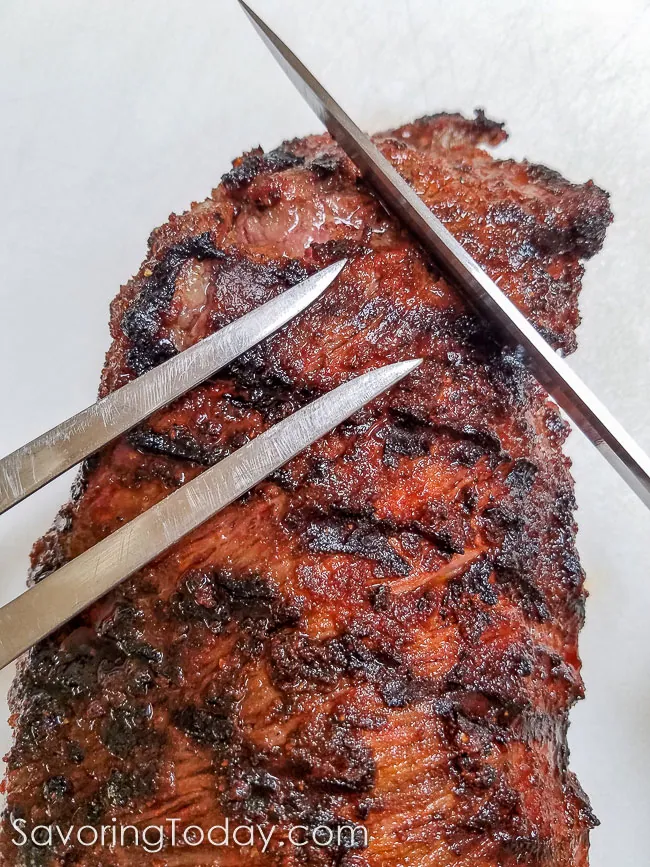 A large fork and knife positioned on a tri-tip roast to show the direction for slicing.