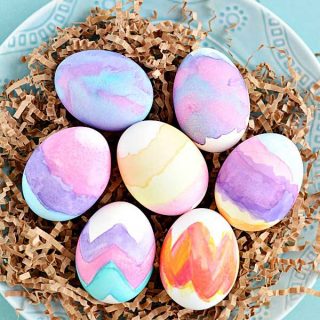 Easter eggs painted with watercolors on brown grass over a blue plate