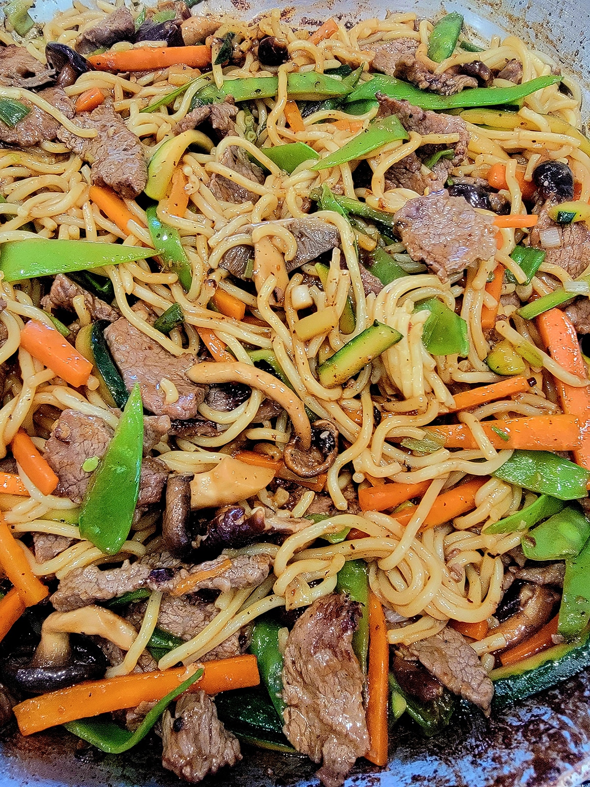 beef, noodles, snow peas, zucchini, carrots, and mushrooms in a skillet