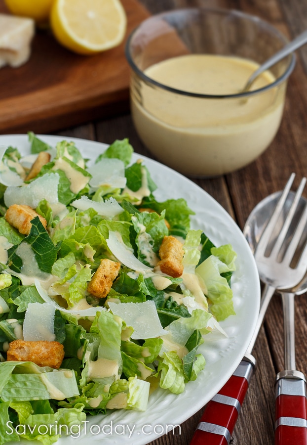 Close-up of Caesar Salad in a white bowl with salad tongs and dressing beside it.