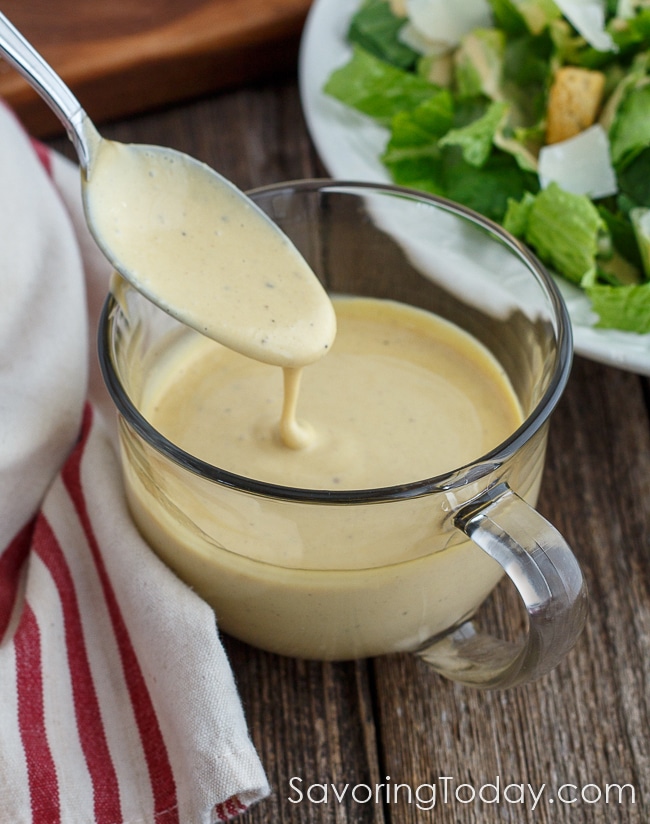Creamy Caesar dressing running off of a spoon into a glass cup.