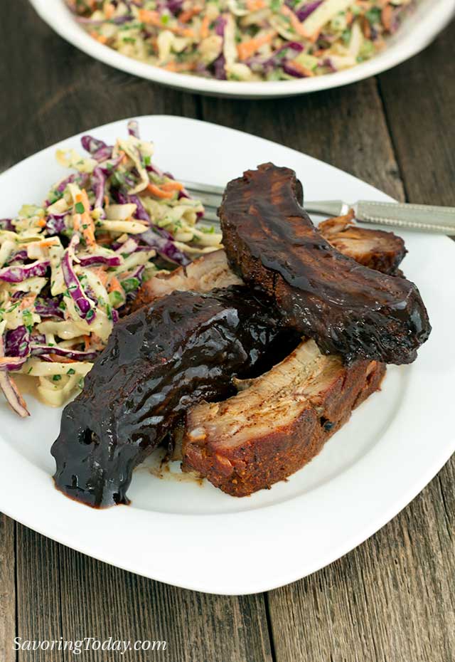 Ribs served dry with rub and with barbecue sauce and coleslaw on a white plate.