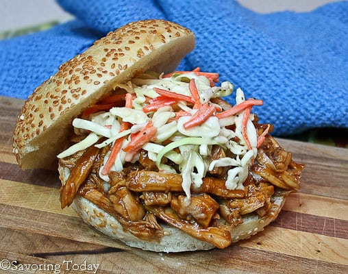 BBQ Pulled Chicken topped with Coleslaw on a bun sitting on a wood board with a blue towel.