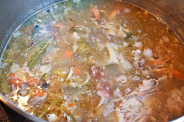 Rich Shrimp Stock with carrots, onion, bay leaf and shrimp carcasses in a stainless steel pot.