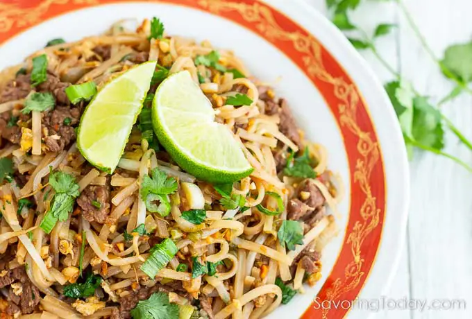Pad Thai with beef and lime in an orange rimmed bowl.