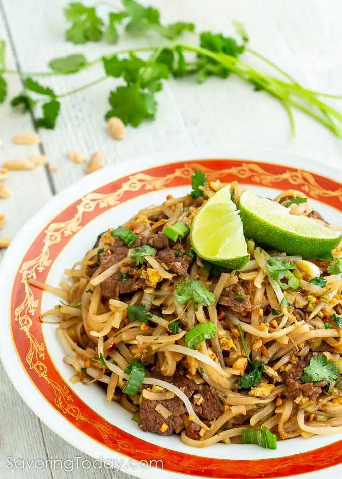 Beef Pad Thai in a bowl with lime wedges on top.