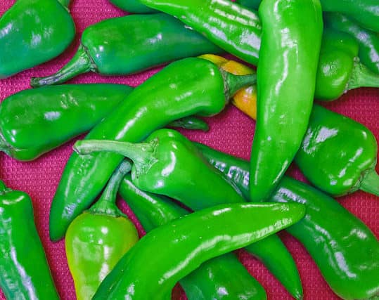 Green chiles in a pile on a pink towel.