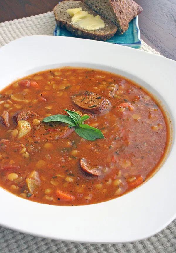 Sausage and split pea stew in a white bowl on a wood table.