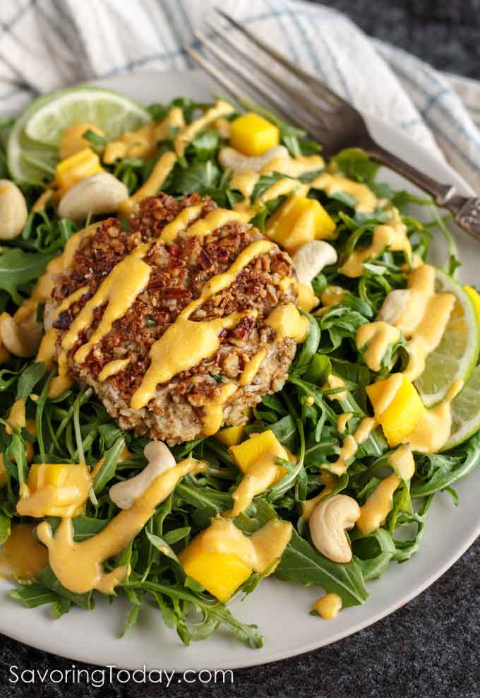 Crab cake on arugula salad greens with mango-lime cashew dressing on a white plate.