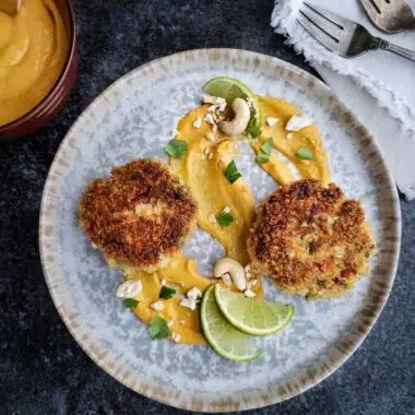 Crab cakes on a swirl of mango-lime cashew sauce with lime wedges.