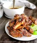 Chicken wings with Thai Chili Sesame Sauce served on a white plate with lime wedges.