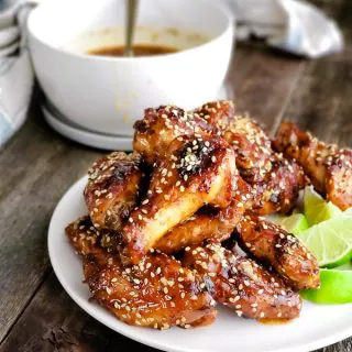 Chicken wings with Thai Chili Sesame Sauce served on a white plate with lime wedges.