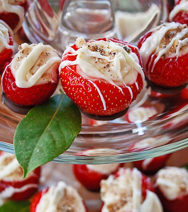 Strawberry with cheesecake filling and white chocolate drizzled on top, on a platter with a green leaf beside it.