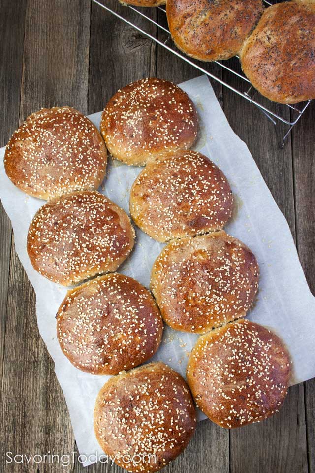 Sprouted wheat burger buns with sesame seeds and poppy seeds on a wood table.