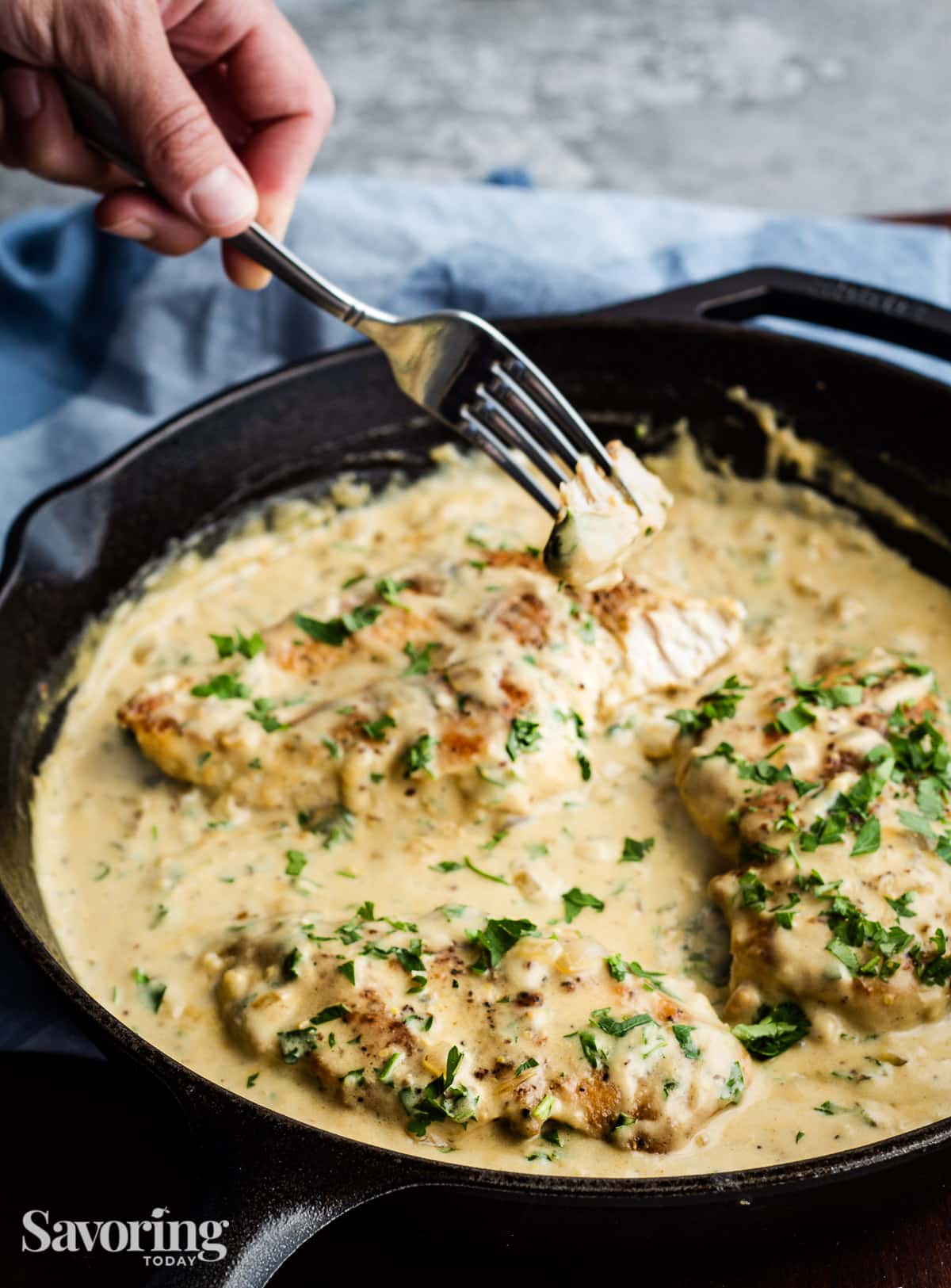 hand holding a fork with a bite of chicken over the skillet of chicken in a creamy sauce