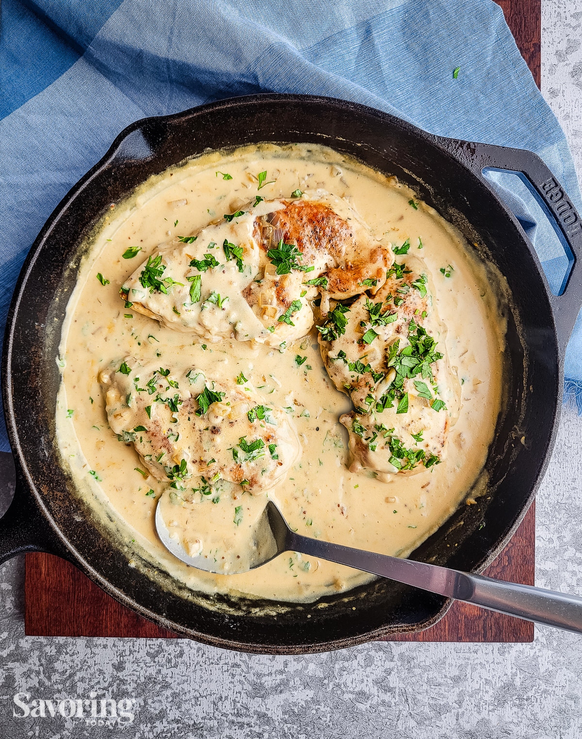 creamy sauce over chicken breasts in a cast iron skillet set over a blue towel