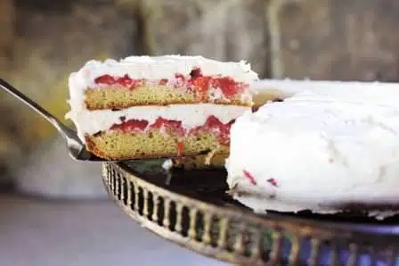 Sliced yellow cake with strawberries and whipped cream icing.