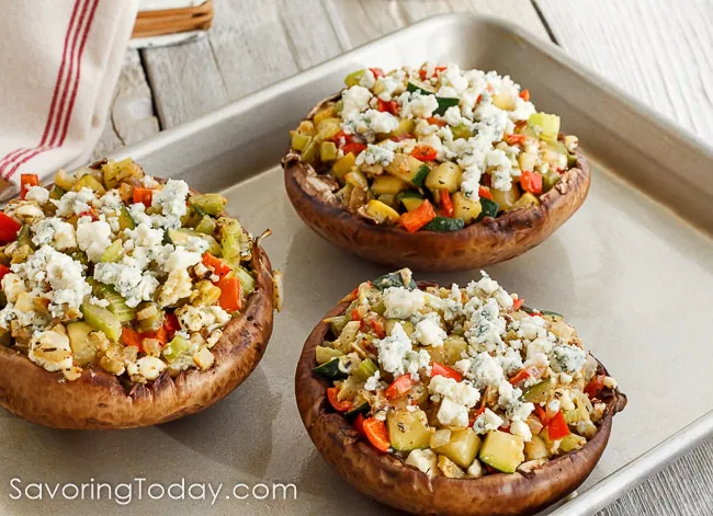 Mushrooms stuffed with vegetables and blue cheese on a metal tray ready for the oven.