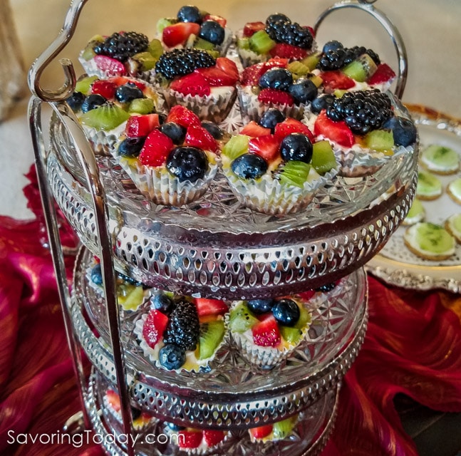 Mini tarts with cream cheese, berries, and kiwi on tiered silver trays.