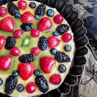 Fruit tart with blackberries, raspberries, blueberries, strawberries and kiwi on a cream cheese filling in a dark tart pan.