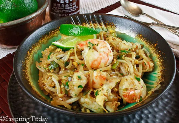 Shrimp Pad Thai in a green bowl with a brown rim set atop a hammered metal plate.