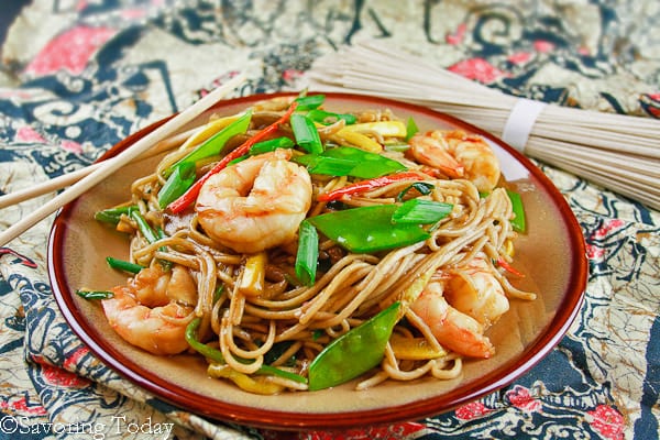 Shrimp and vegetables with lo mein  noodles and sauce with dry soba noodles in the background. 