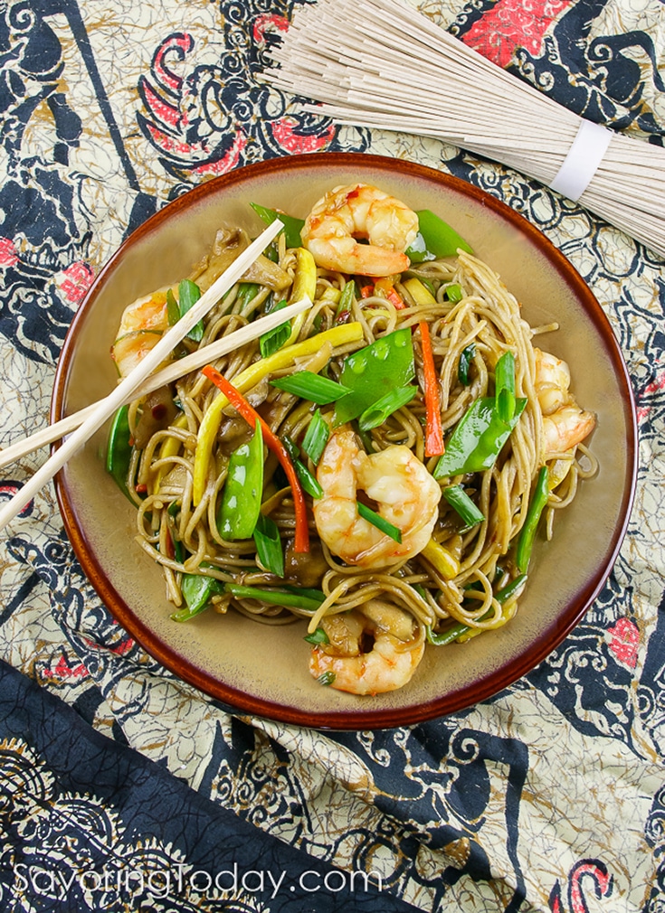 shrimp and vegetables with lo mein noodles on a plate with chop sticks