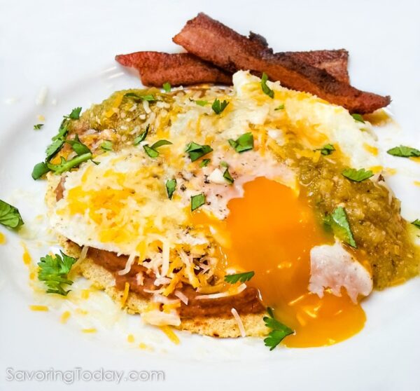 Huevos rancheros on a white plate with the egg yolk running over the side of the stack.