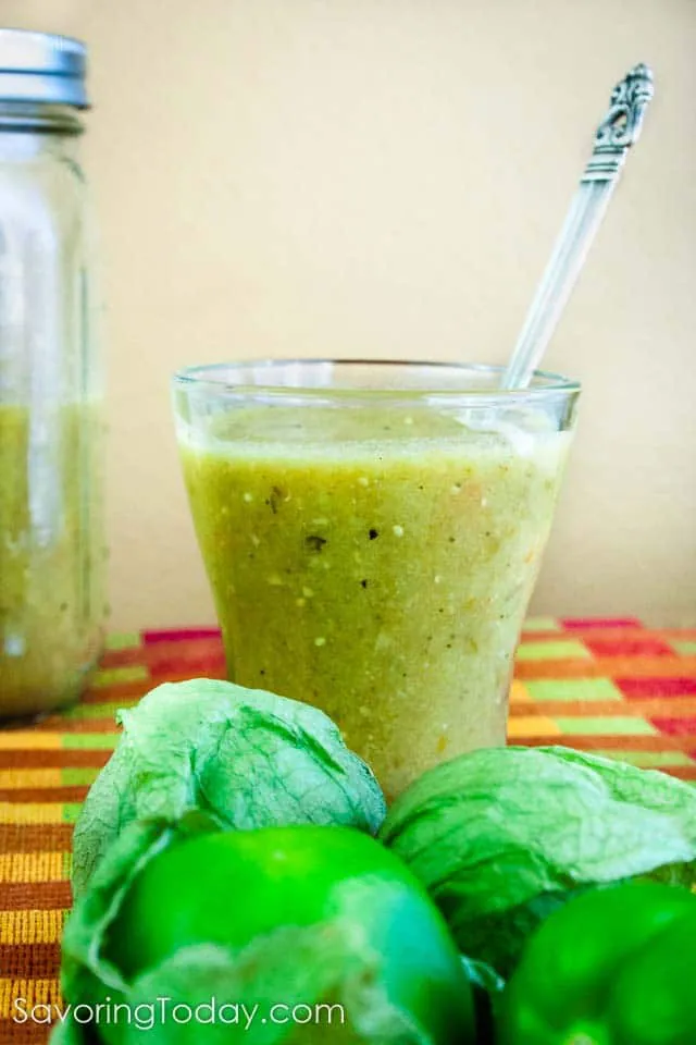Tomatillo-Green Chile Sauce in a clear glass with a spoon with fresh tomatillos.