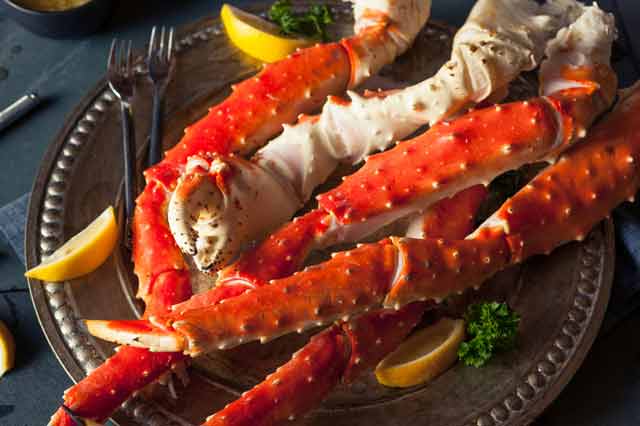 King crab legs on a metal platter with lemon slices and crab forks.