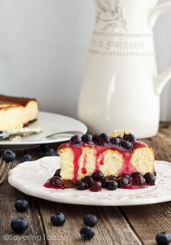 New York Cheesecake with blueberry topping on a white plate sitting on a table