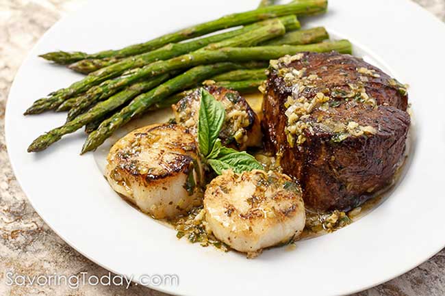 Close-up of filet mignon and scallops with a basil leaf garnish with asparagus.