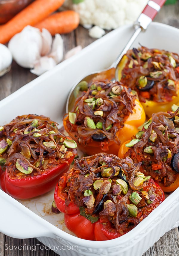 Stuffed red and yellow bell peppers topped with caramelized onions and pistachios in a white ceramic baking dish and serving spoon. 