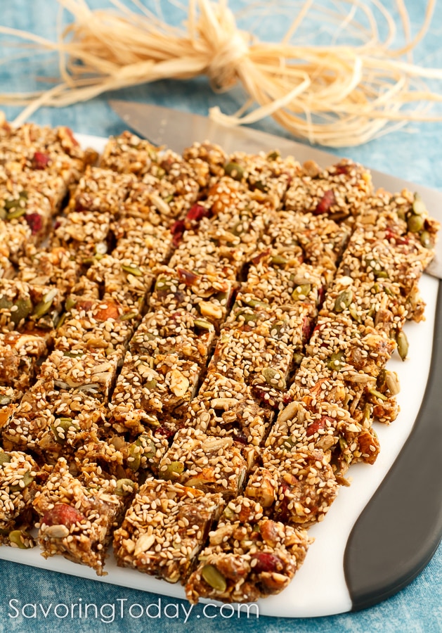 Granola snacks cut into 1 inch squares on a cutting board over a blue background.