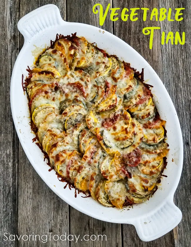 Vegetable gratin with a cheese topping from the oven in a white baking dish on a wood table.