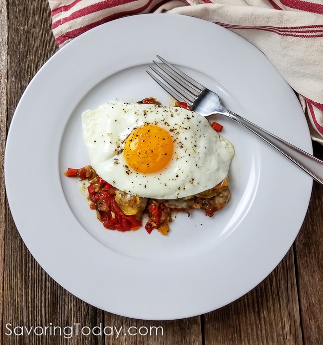Sunny side up egg over roasted vegetables on a white plate with a red striped towel.