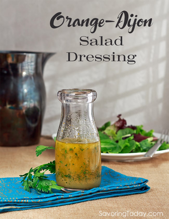 Orange-Dijon salad dressing with specs of parsley in a glass bottle on a blue cloth napkin.