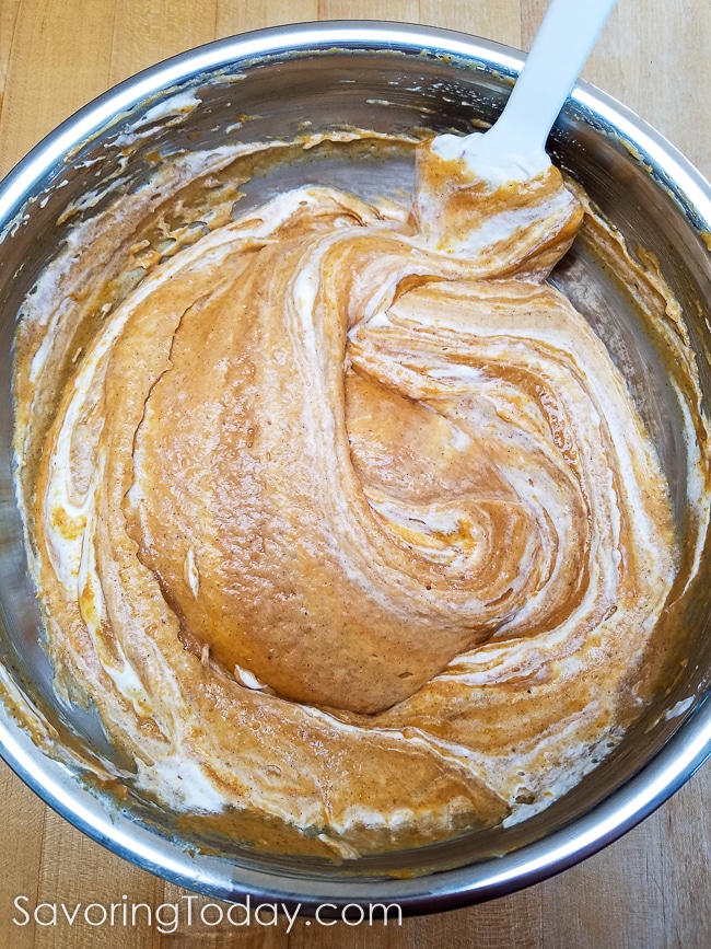 Real whipped cream folded into pumpkin pie custard in a metal bowl.