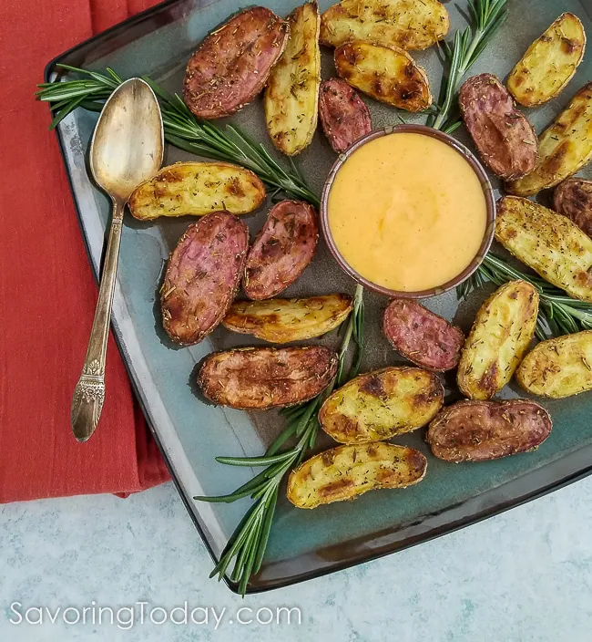 Roasted fingerling potatoes served on a blue platter with fresh rosemary and gochujang aoili for dipping. 